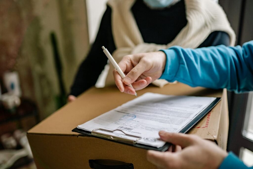 Close-up of a person signing a delivery document placed on a large cardboard box indoors.